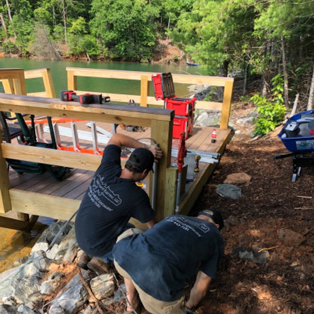 Men constructing a wooden dock by the water, surrounded by trees and tools.